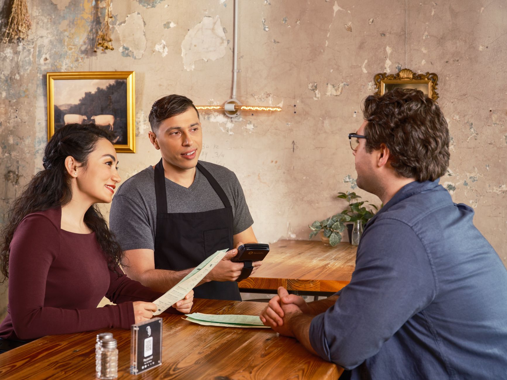 A server holding a handheld card terminal beside a table, with both guests looking at it.